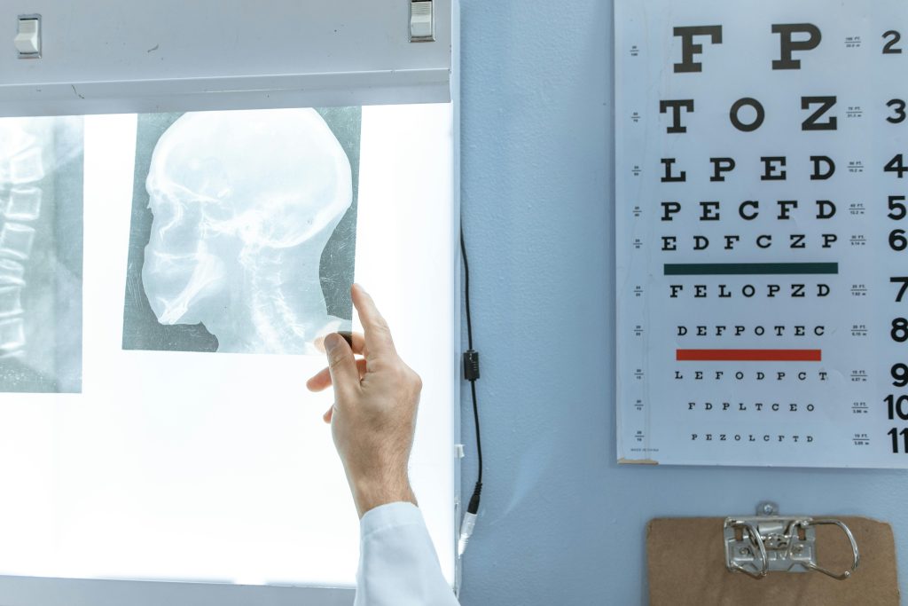 Home A medical professional checks an X-ray next to a Snellen eye chart in a clinic.